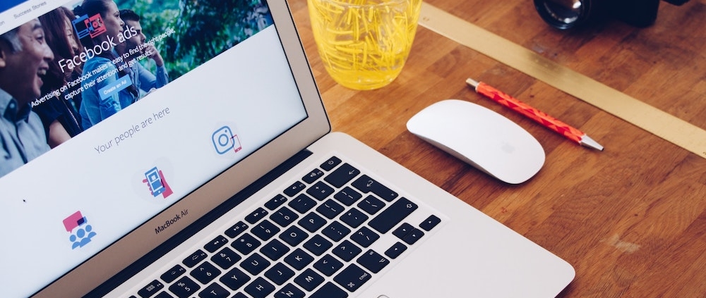 A laptop, cordless mouse, yellow glass, pen, and camera on a wooden table.